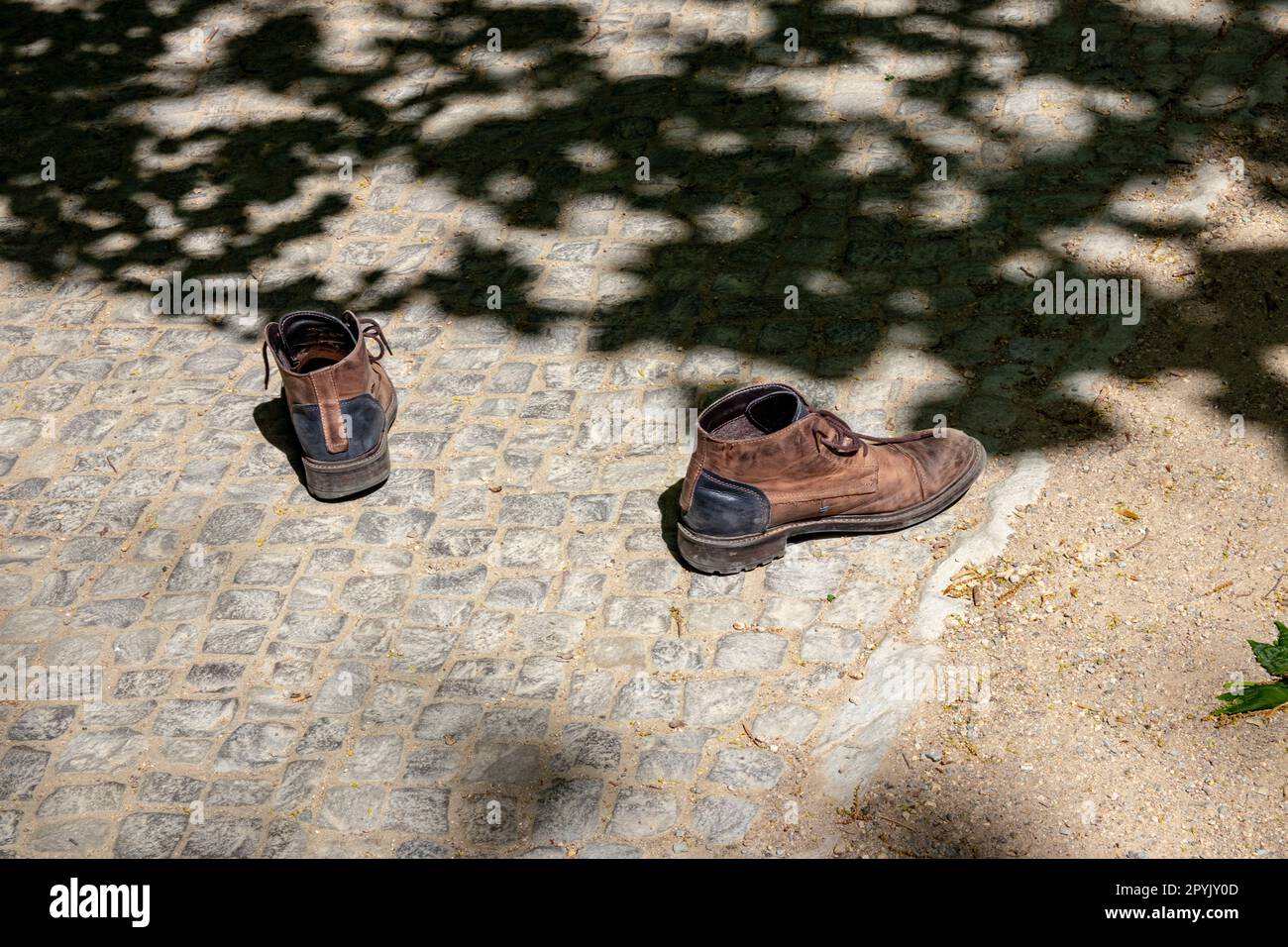 A pair of old worn brown walking shoes left behind on the path. Abandoned shoes on the way. Stock Photo