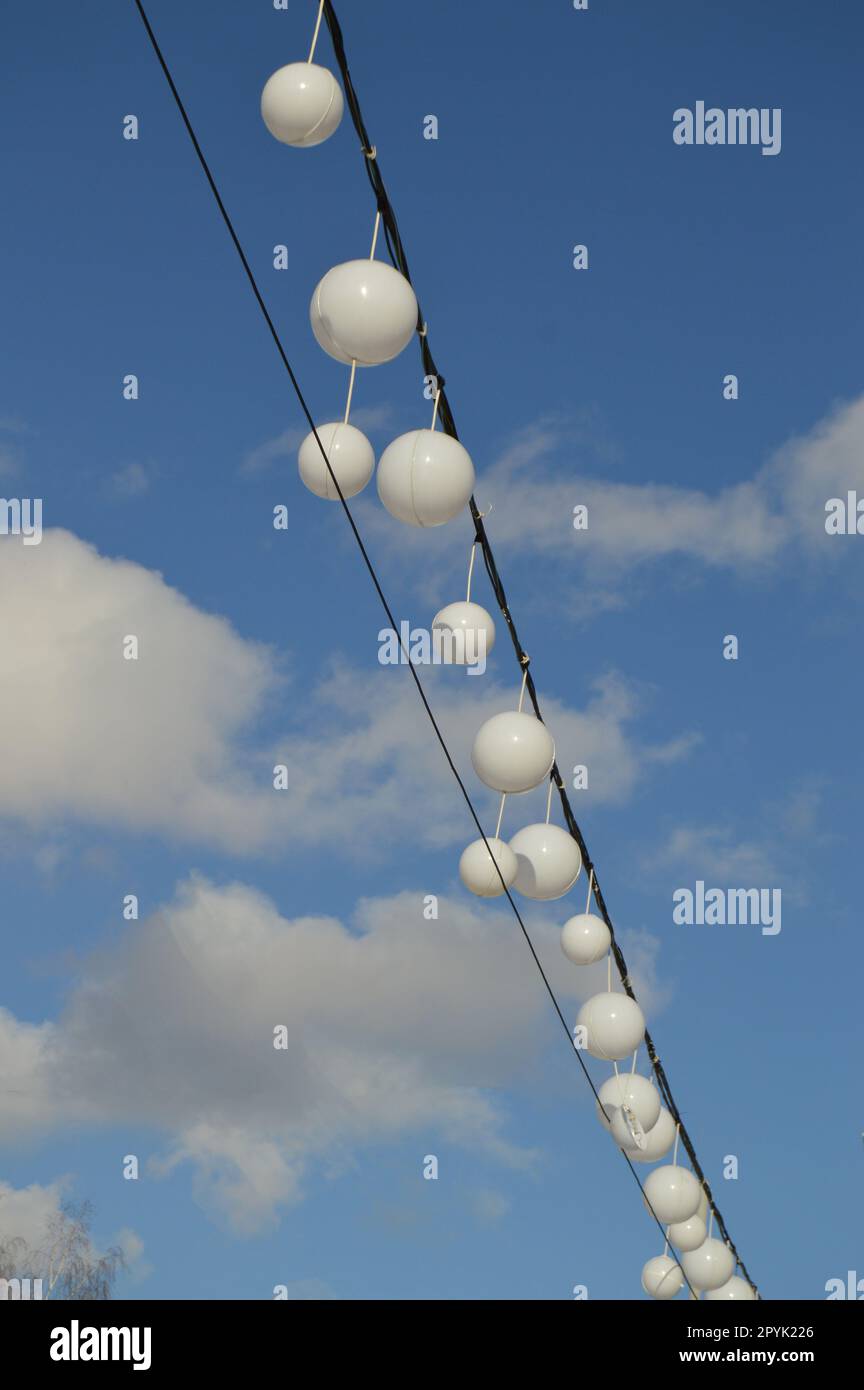 White garland balloons oscillate in the wind against blue sky and clouds, peaceful landscape, vertical, shot Stock Photo