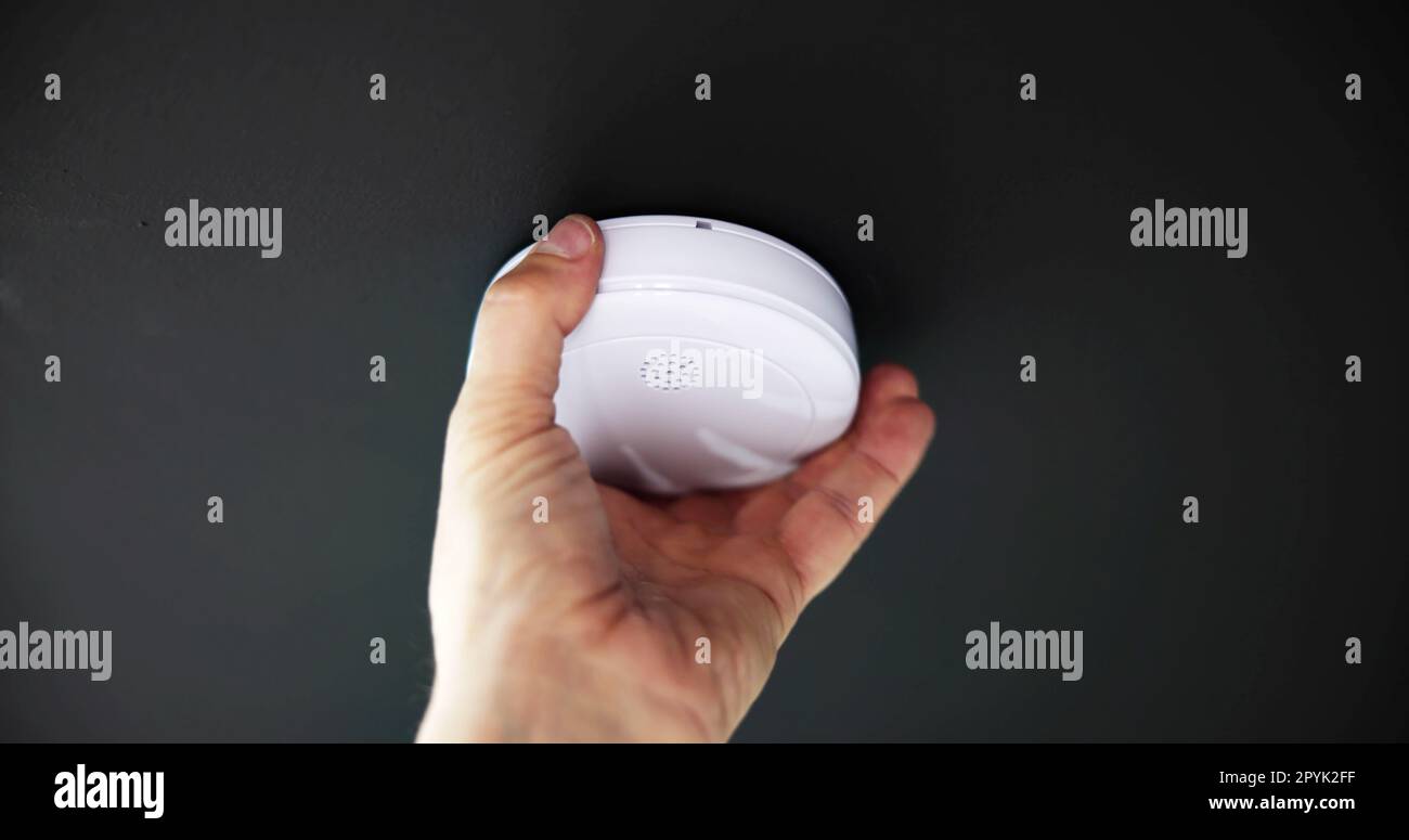 Person's Hand Installing Smoke Detector On Ceiling Wall Stock Photo