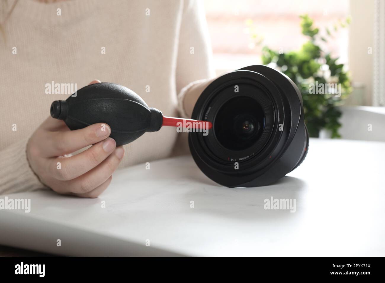 Cleaning digital camera lens, hands cleaning dust from front of lens with a special cleaning kit airbomb on desk Stock Photo