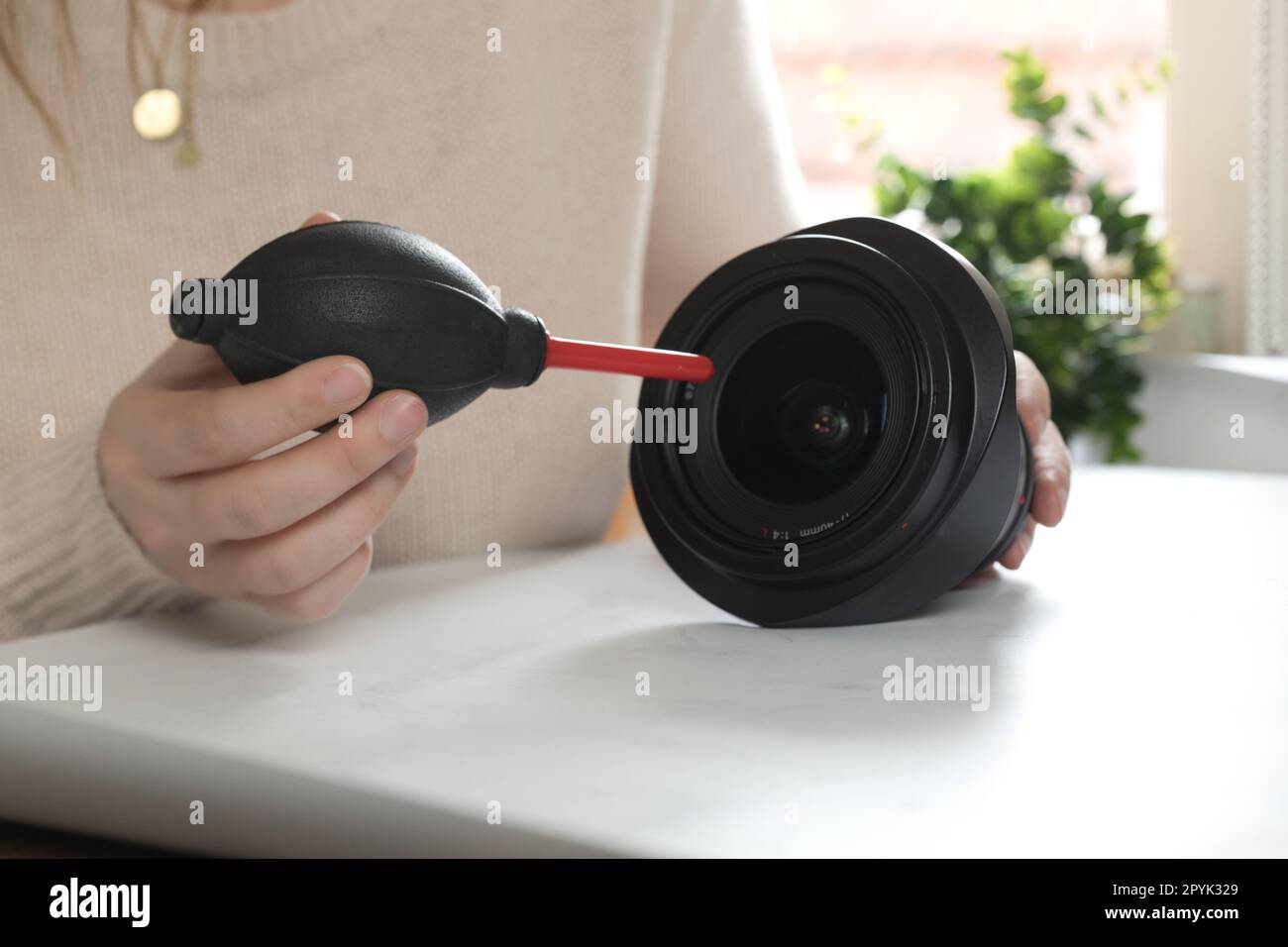 Cleaning digital camera lens, hands cleaning dust from front of lens with a special cleaning kit airbomb on desk Stock Photo