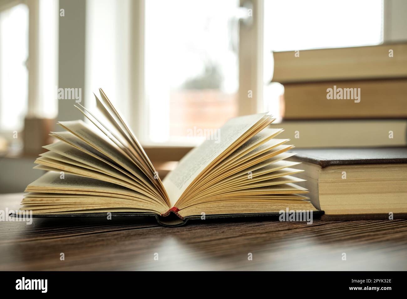 Education learning concept with opening book or textbook at home in office room, stack piles of literature text academic archive on reading desk and aisle of bookshelves in school study class room background interior Stock Photo