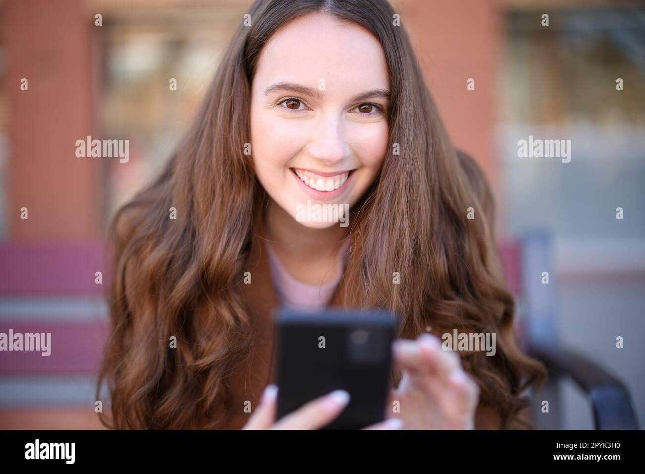 Happy woman on a bench looks at you holding phone Stock Photo