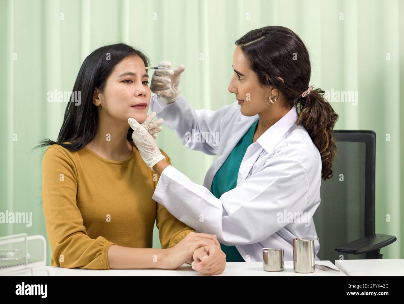 Doctor in white gown and protective glove giving female patient medical injection in forehead. Stock Photo