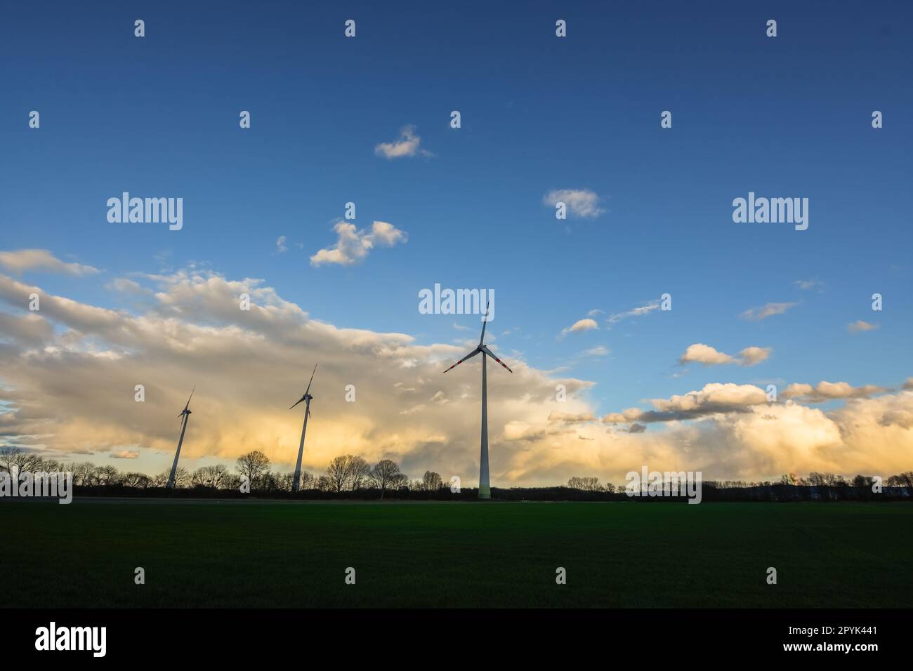 colorful rainclouds with blue sky and a flat landscape with three windmills Stock Photo
