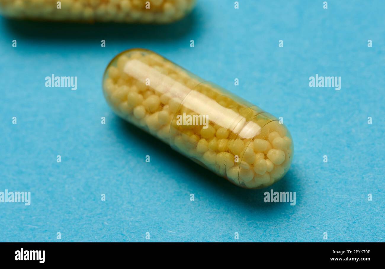 Transparent medical capsules with yellow granules inside on a blue background, tablets for treatment, vitamins Stock Photo