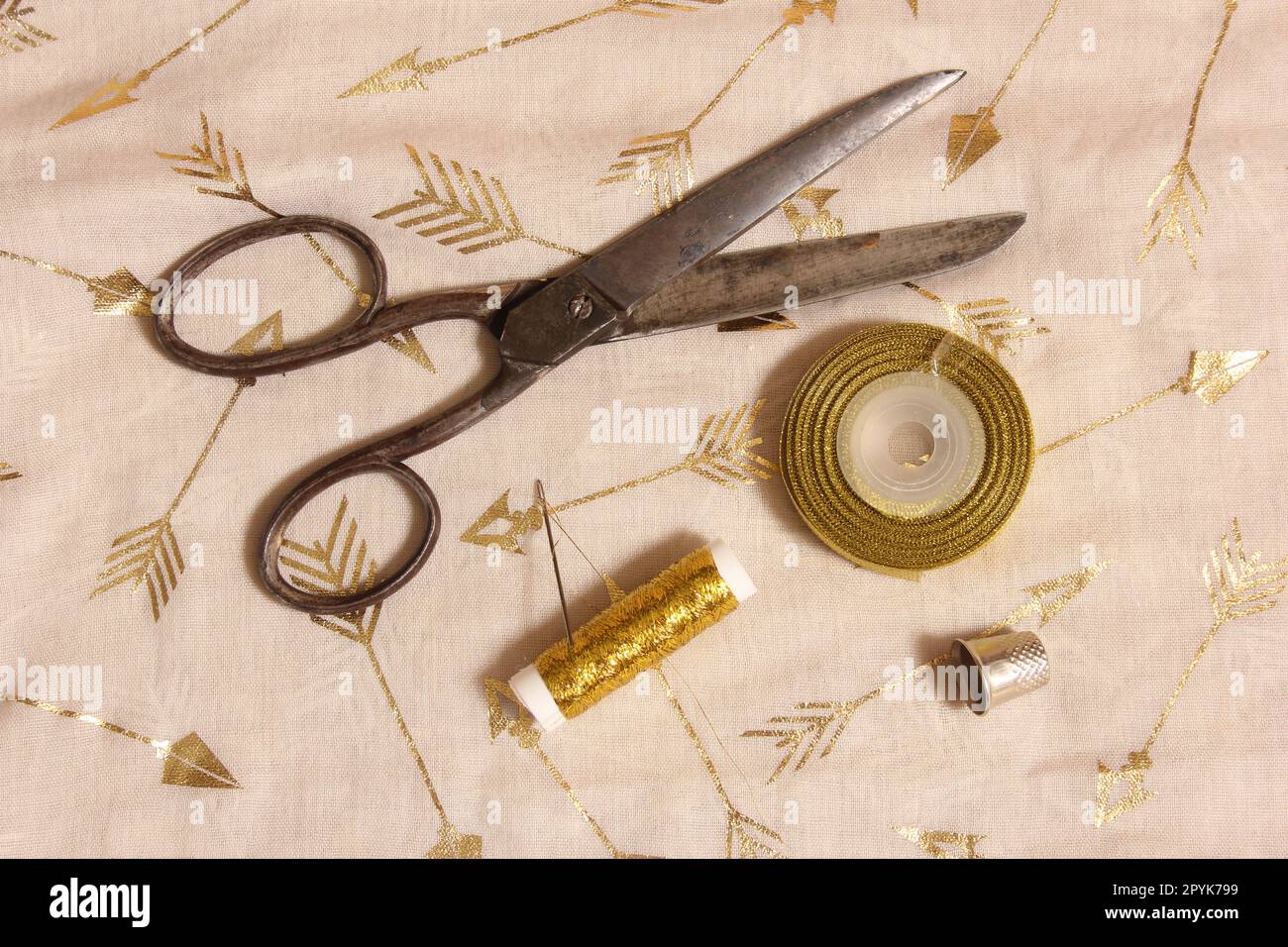 Spool of Gold Thread and Scissors With Thimble on Metallic Chiffon Fabric Stock Photo