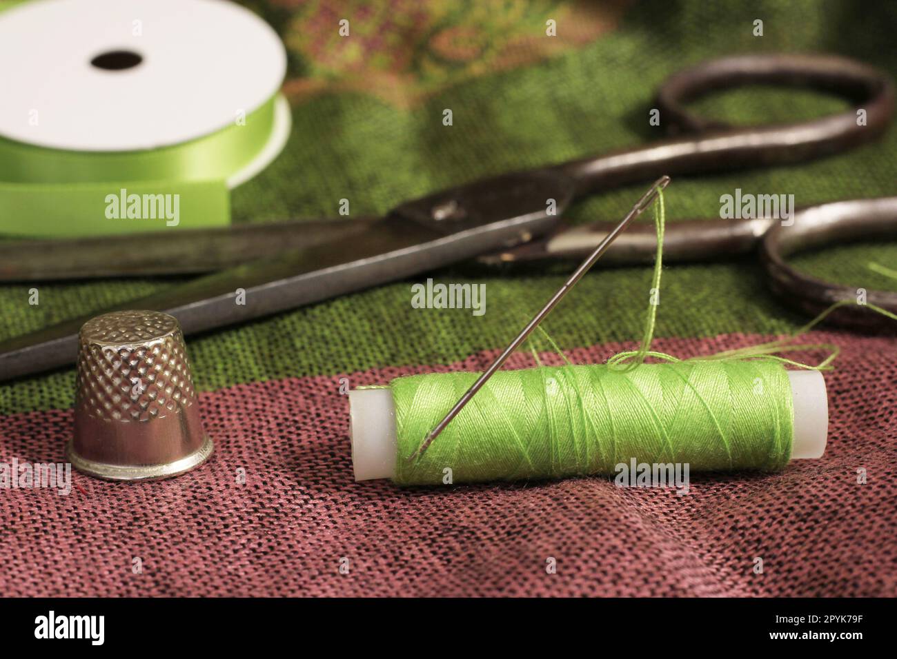 Spool of Green Thread, Thimble and Needle on Antique Green and Pink Fabric Stock Photo