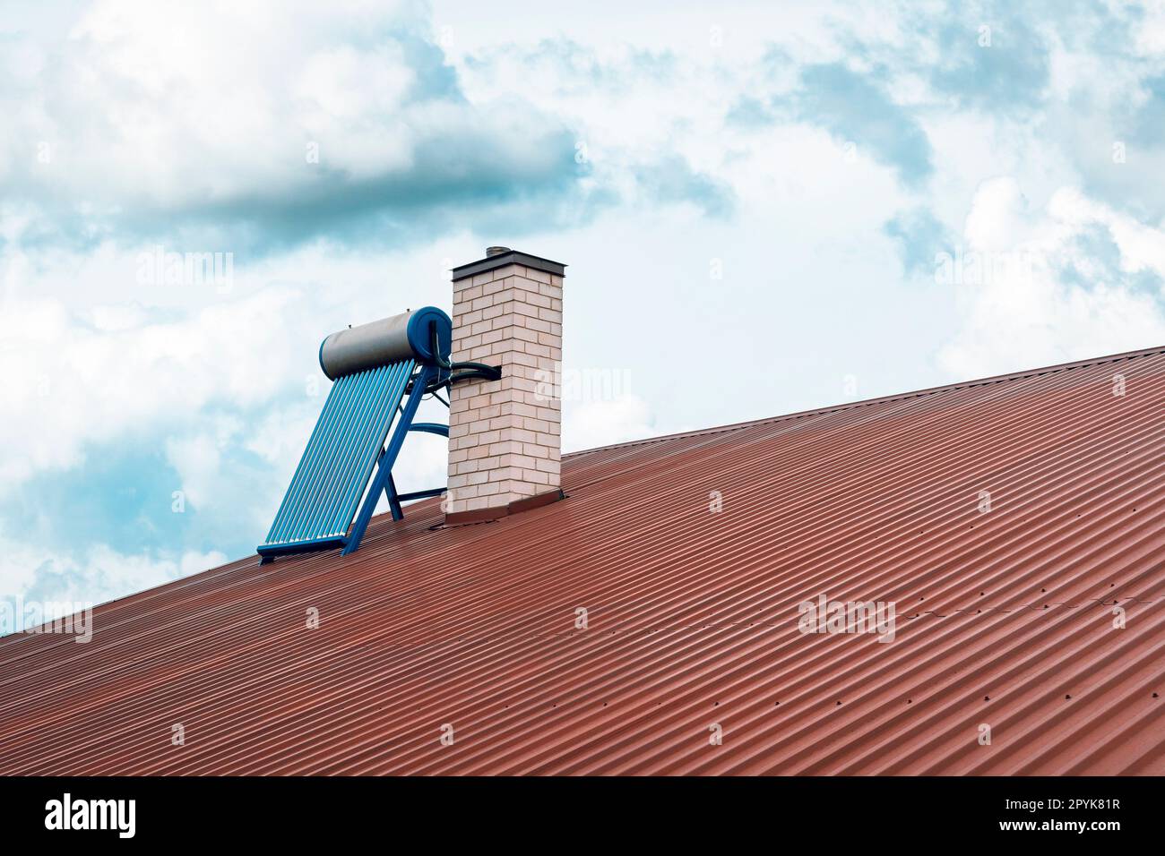 Solar water heater installed next to chimney on a red roof Stock Photo