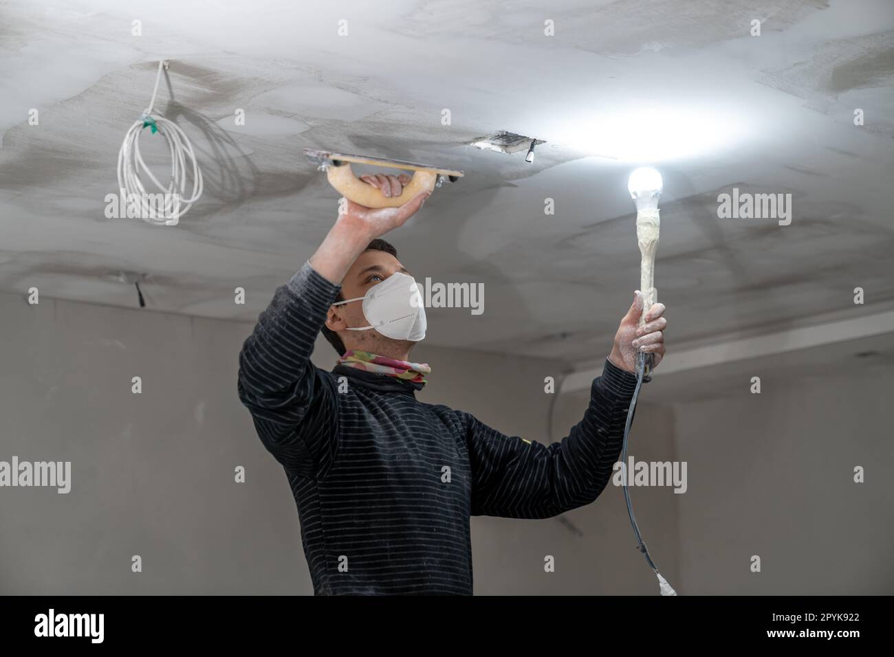 sanding a plasterboard ceiling in a new building with a trowel Stock Photo
