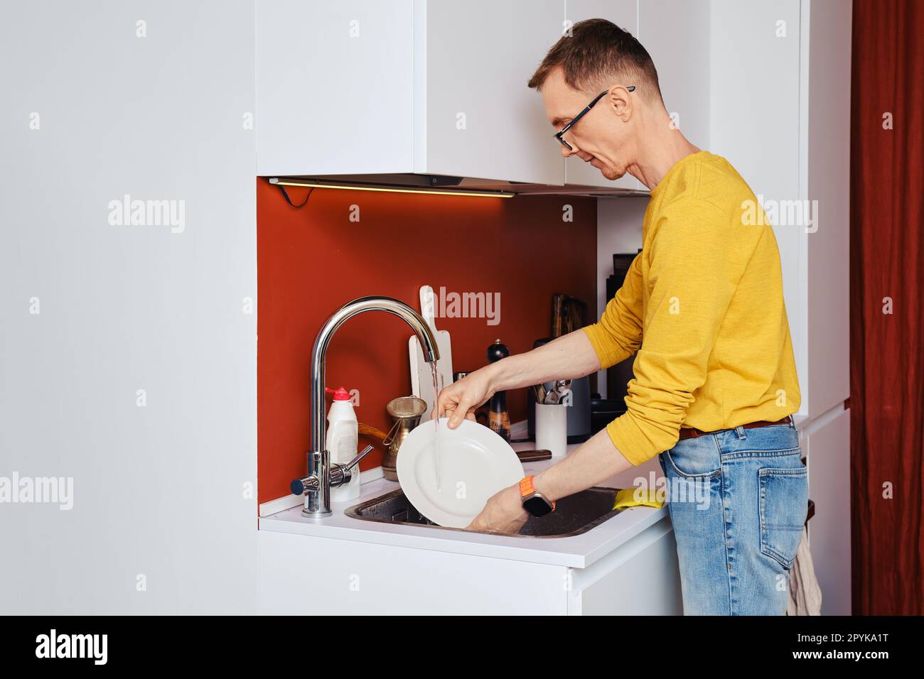 Middle-aged man washing plate after dinner in kitchen Stock Photo