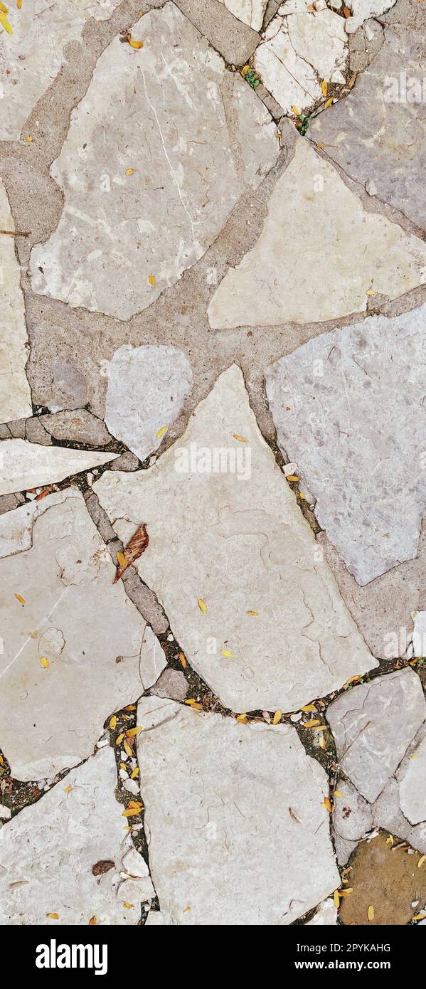 pavement paved with uneven natural gray and brown stones. Between crushed cobblestones there are small pebbles, earth, sand, grass. Solar lighting. Square in the old european city Stock Photo