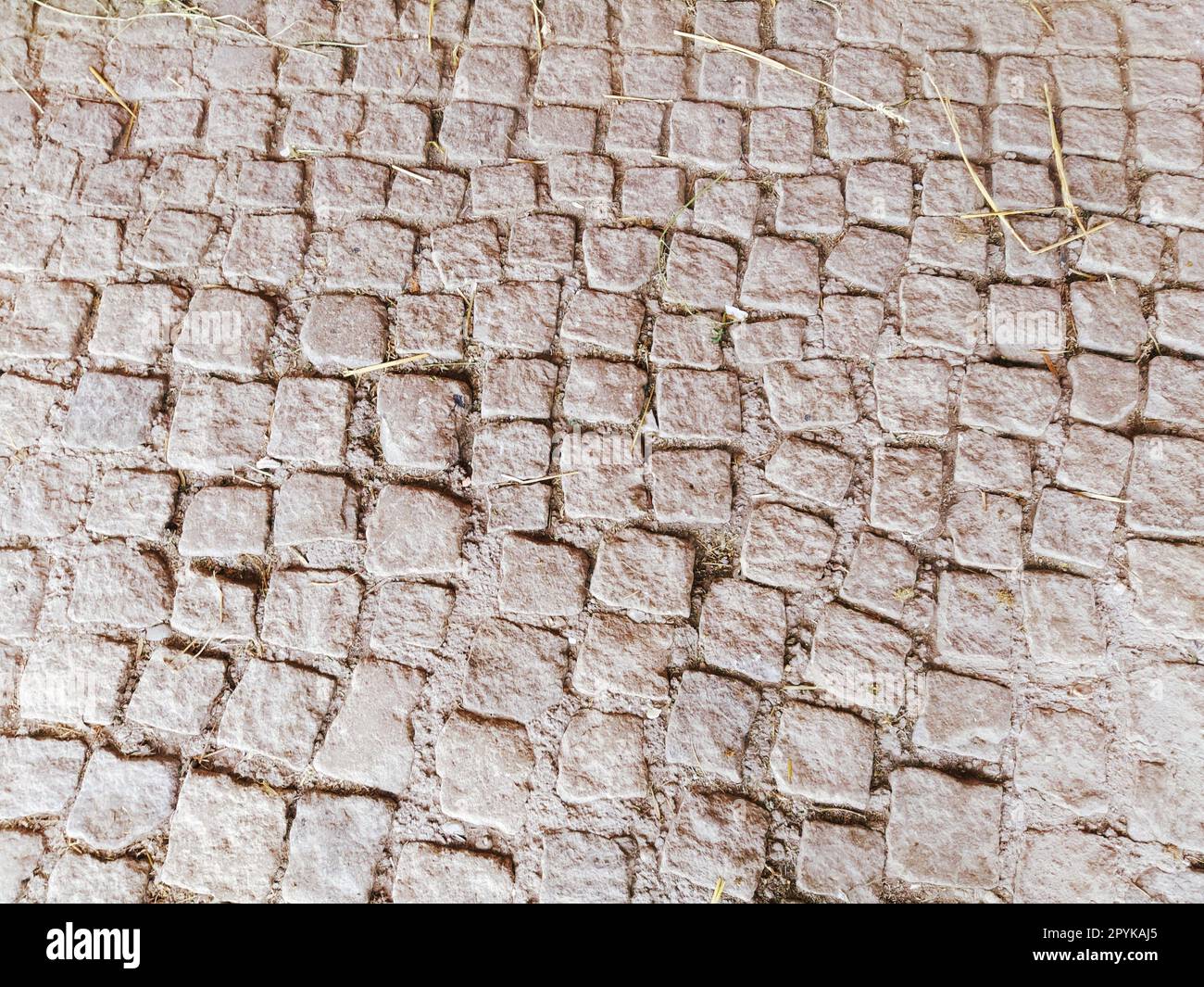 pavement paved with uneven natural stones. Between crushed cobblestones there are small pebbles, earth, sand, grass. Square in the old european city. Brown sepia effect Stock Photo