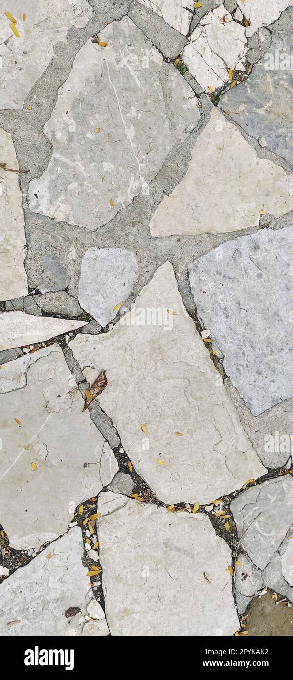 pavement paved with uneven natural gray and brown stones. Between crushed cobblestones there are small pebbles, earth, sand, grass. Solar lighting. Square in the old european city Stock Photo