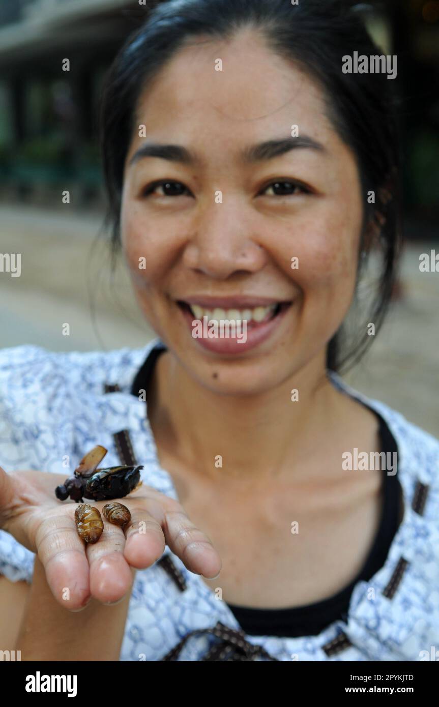 A Thai woman eating a fried grasshopper in Bangkok, Thailand. Stock Photo