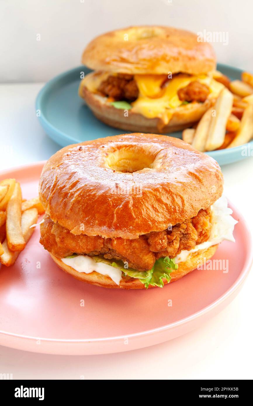 Crispy breaded fried chicken brioche donut bun burger served with hand cut fries on pink plate. Stock Photo