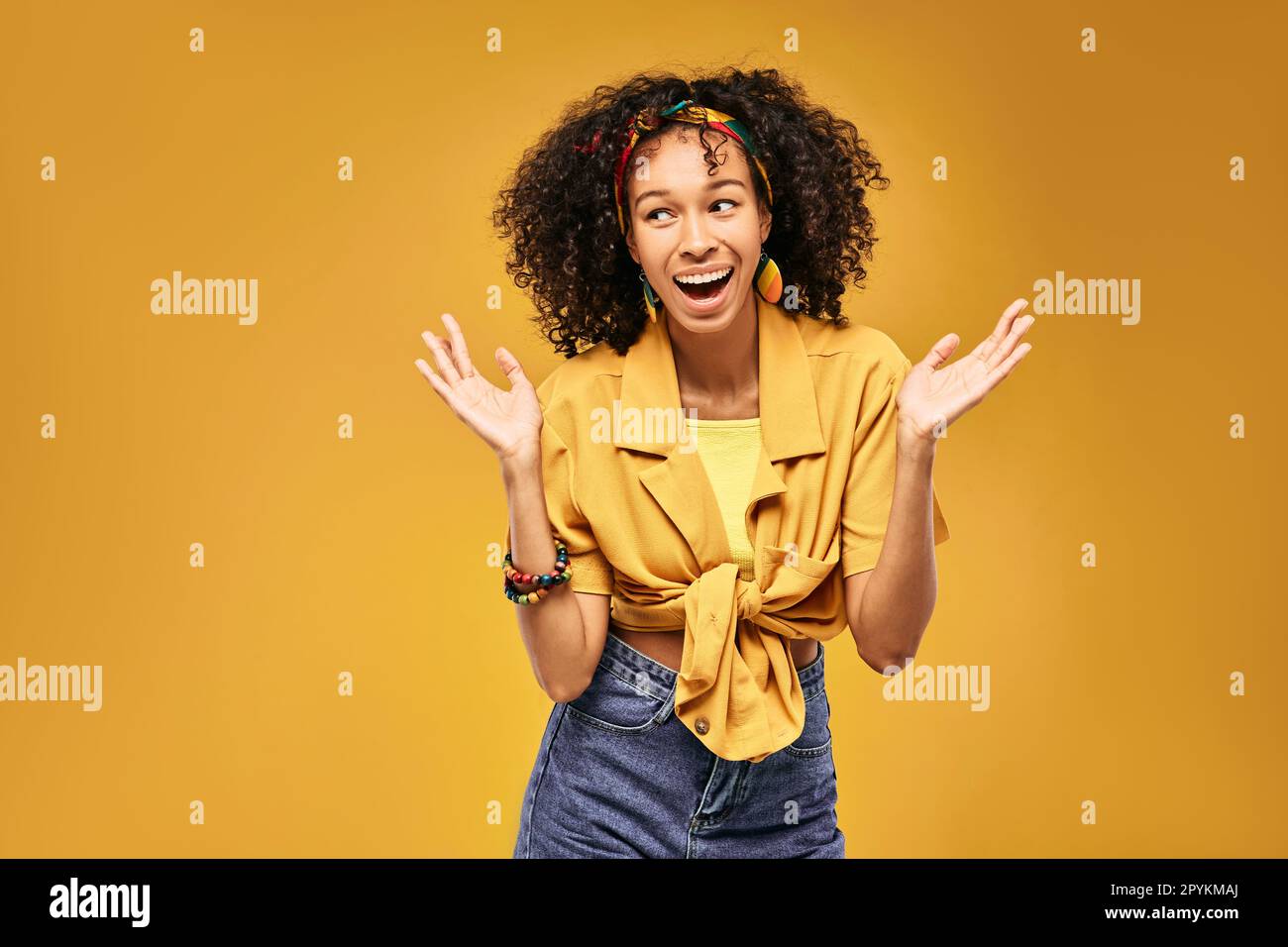 Emotion of surprise on African American woman face with hands above head, she can't believe her happiness, on yellow background Stock Photo