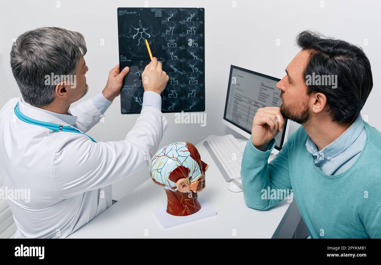 Man with migraine and headache at consultation with neurologist who looking at MRA of patient's head to analyze his brain health. Cerebrovascular MRI Stock Photo