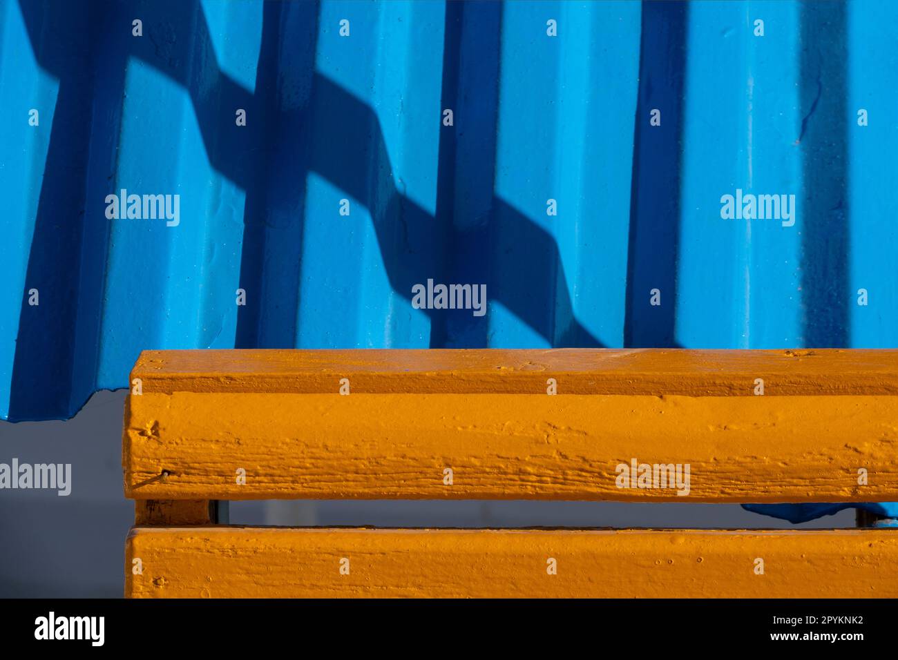 Bright blue corrugated roofing panel with bright orange pained timber in front with diagonal