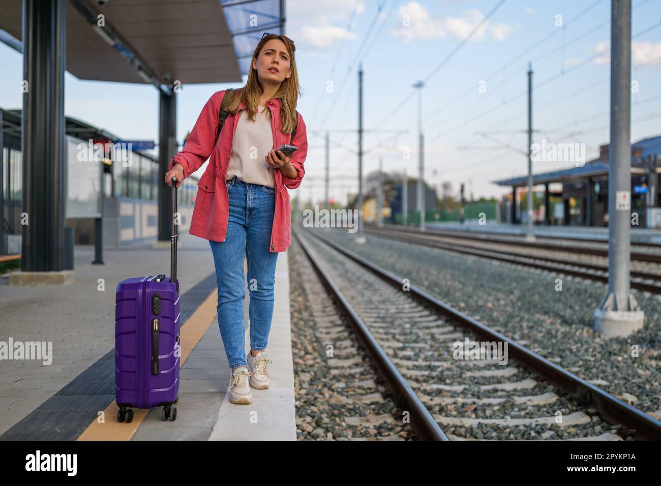 Adult woman is standing at railway station and waiting for arrival of train. Stock Photo