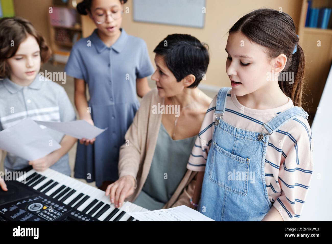 Choir of children singing songs in music class while teacher playing