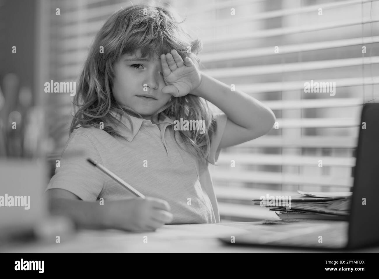 Tired sad school boy while doing homework. Child hold a pencil and draw