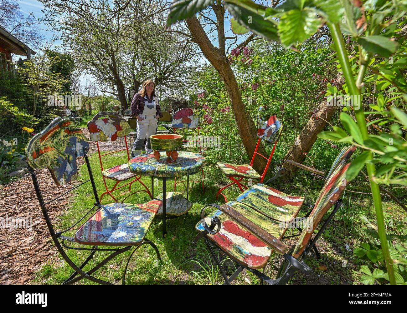 04 May 2023, Brandenburg, Sieversdorf: Undine Gomille, artist, stands next to ceramic chairs and tables and prepares the garden for the 'Open Studio Days'. The first weekend in May has become a fixed date for many art enthusiasts over the past few years. On May 06 and 07, 2023, artists will again open their studios in Brandenburg's counties and independent cities. Those who like can discover painting, graphics and book art directly at the place of origin, can look over the shoulder of sculptors and ceramic artists, learn to understand printing techniques and in some places even get the opportu Stock Photo