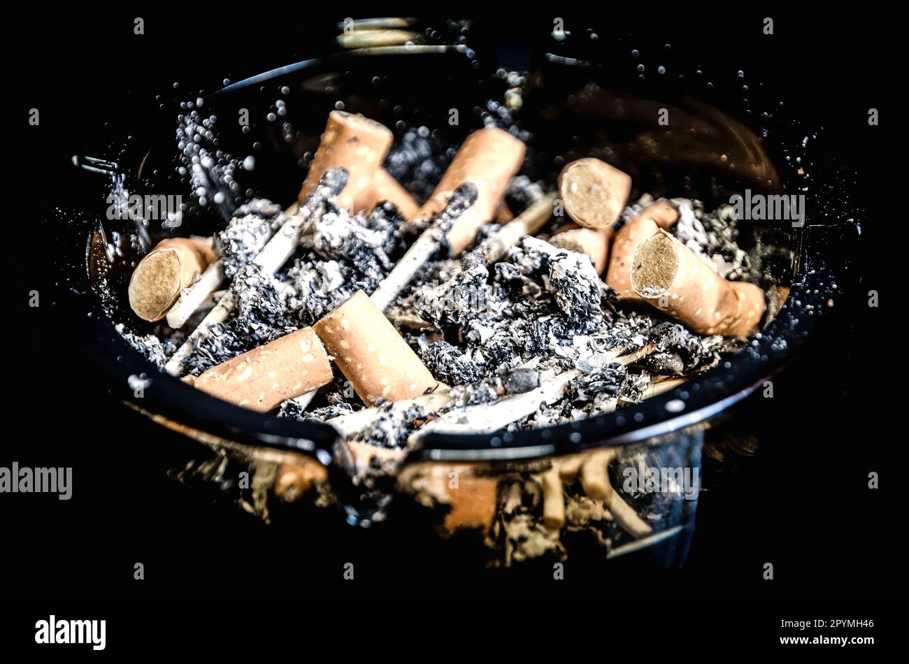 Overhead of burning cigarette in ashtray on black background. Photo