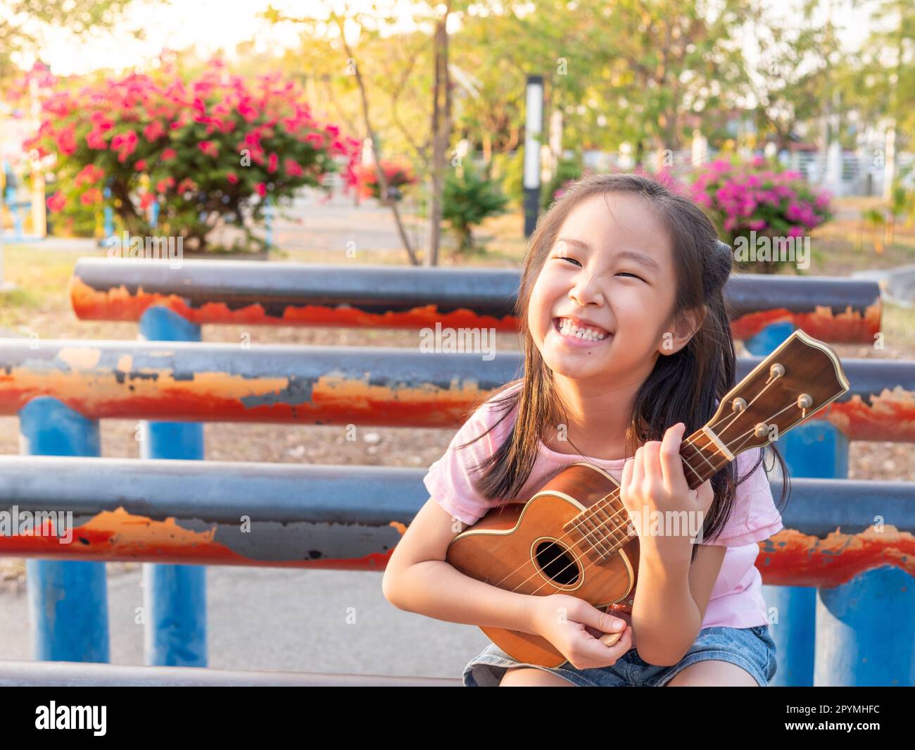 Little asian child girl play the ukulele, in the garden on the Steel