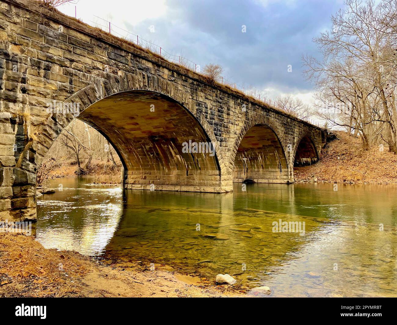 The Cacapon River flows beneath a historic stone railroad bridge used by freight trains and Amtrak passenger trains near the Potomac River. Stock Photo