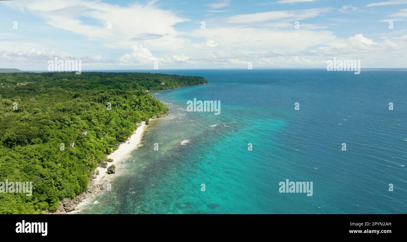 Beautiful sandy beach on a tropical island with abundant green trees along with a small rock formation in the shore. Stock Photo