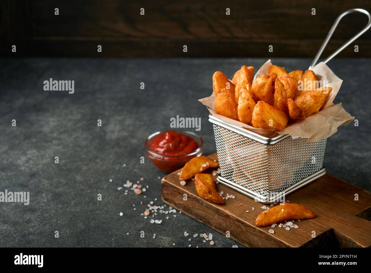 French fries in metal wire basket with salt and ketchup on old wooden