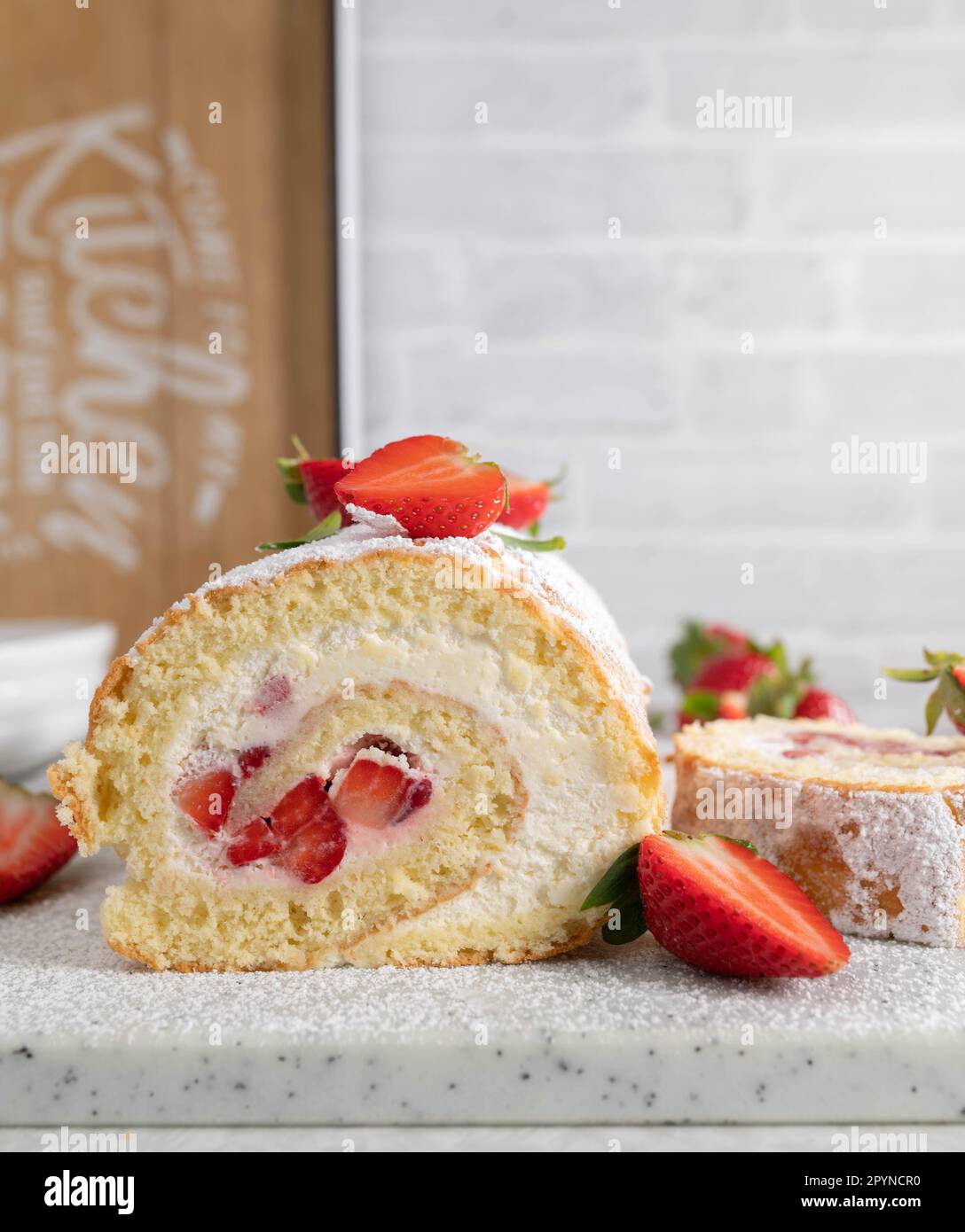 Summer Strawberry dessert with fresh baked swiss roll filled with whipped cream and marinated strawberries. Served on white kitchen table background Stock Photo