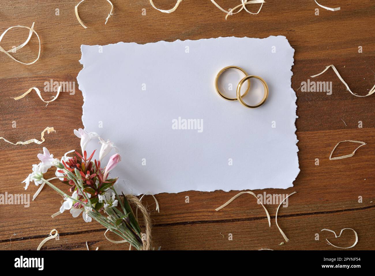 detail of two gold rings on a rustic wooden table with straw and sackcloth for decoration and a white isolated background front view 2PYNF54