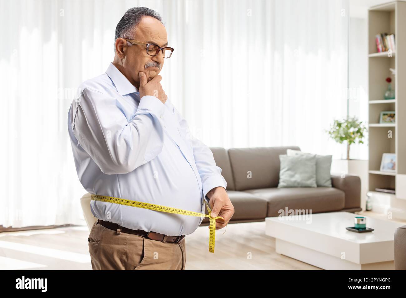Worried mature man measuring his waist in a living room at home Stock Photo