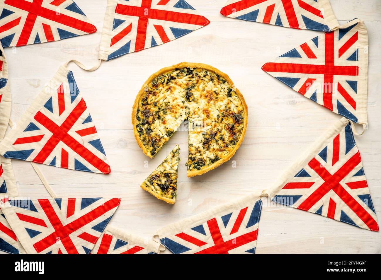 Coronation Quiche on white wooden background surrounded by Union Jack bunting. Official recipe launched for the coronation of King Charles III 2023. Stock Photo