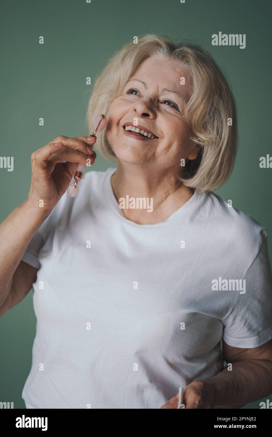 Senior woman of 50s massaging face skin using natural facial stone jade