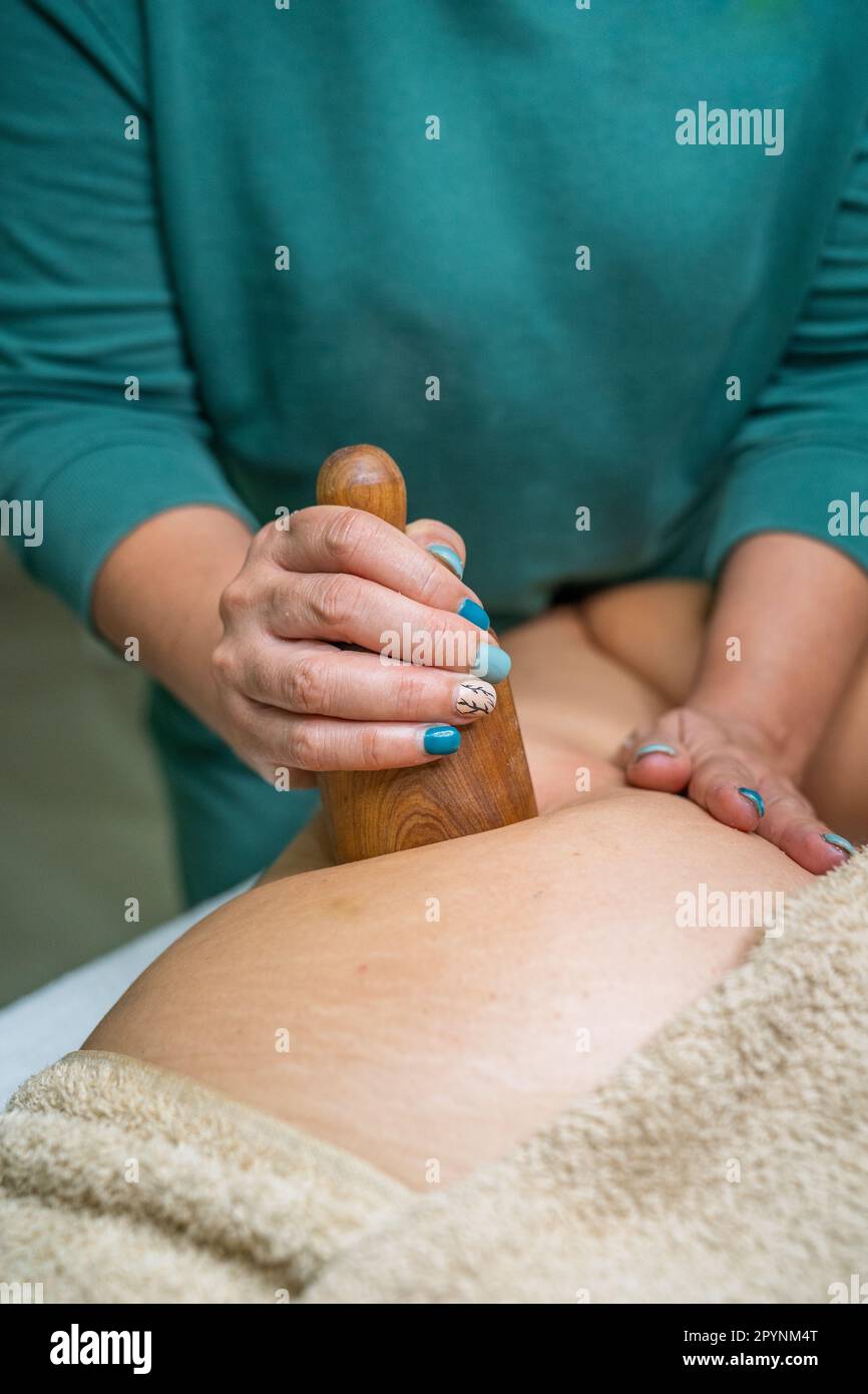Beautician performing wood therapy treatment on the patient's buttock with the instrument of the wooden cup. Close up. Stock Photo