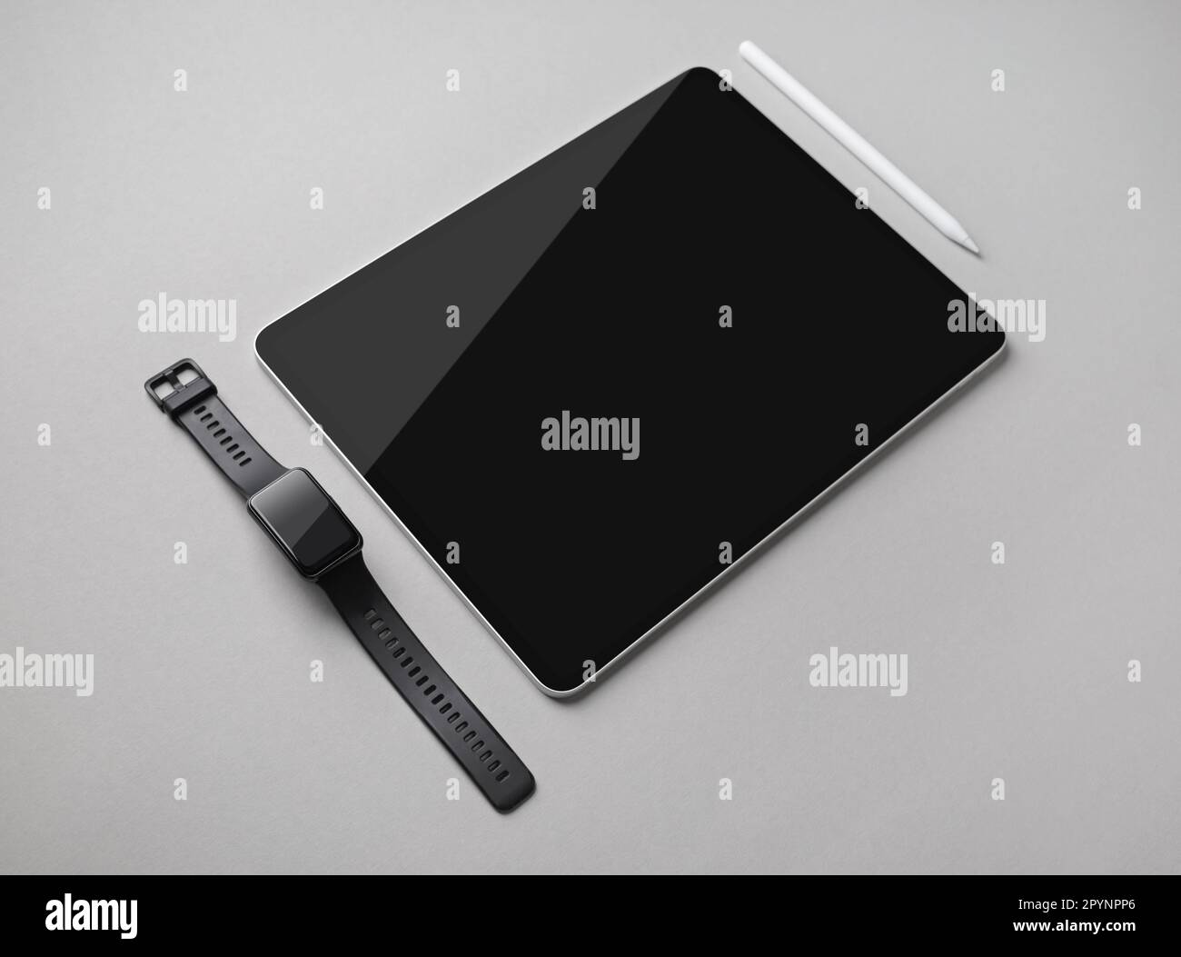Digital tablet with blank black screen, fitness bracelet and stylus pen on gray paper background. Stock Photo