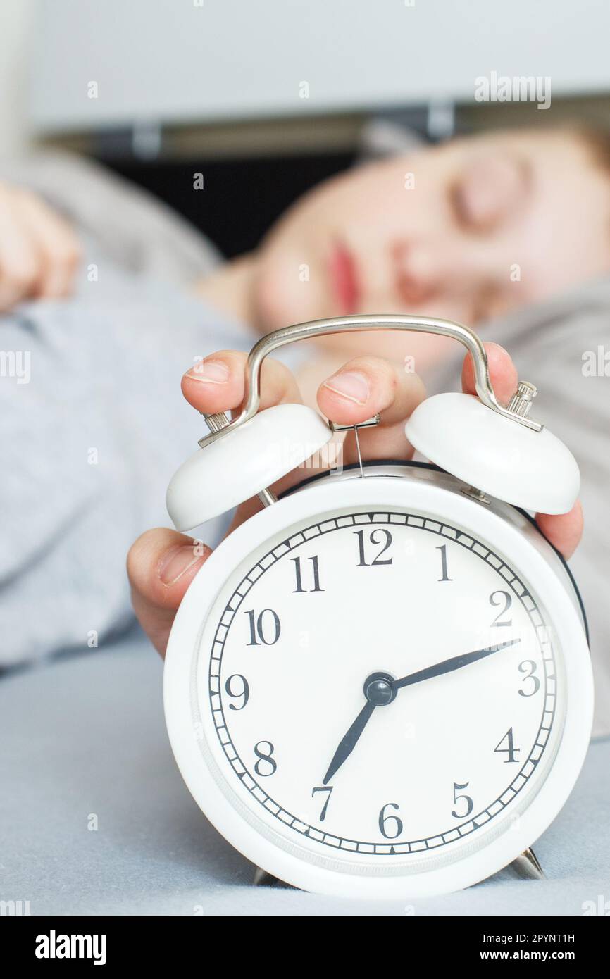 boy lying on bed and stopping alarm clock in morning. childs hand