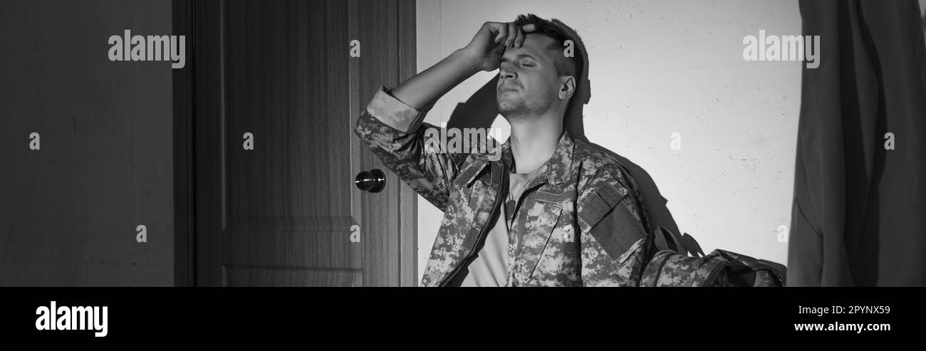 Black and white photo of depressed military veteran sitting in hallway at home, banner,stock image Stock Photo