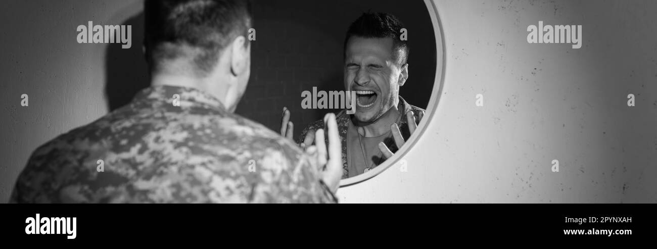 Black and white photo of stressed soldier with emotional distress screaming near mirror at home, banner,stock image Stock Photo