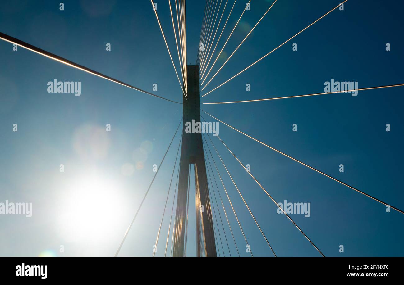 Suspension bridge support cables against a blue sky and sunbeam reflections Stock Photo