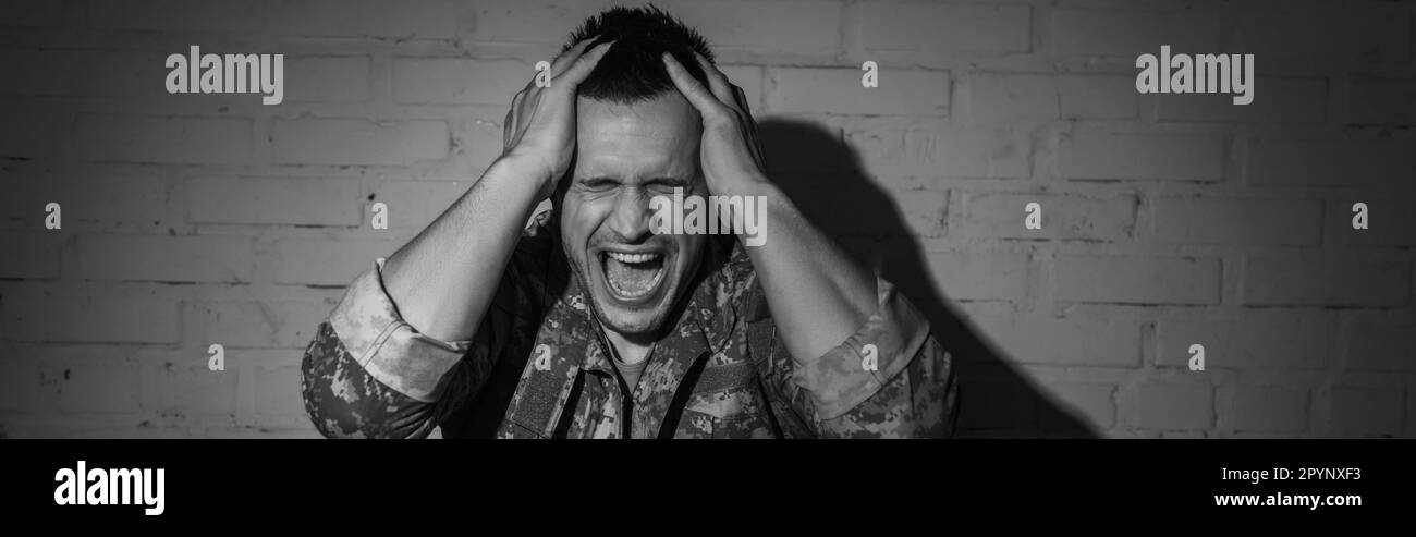 Black and white photo of stressed military veteran screaming while suffering from post traumatic stress disorder at home, banner,stock image Stock Photo