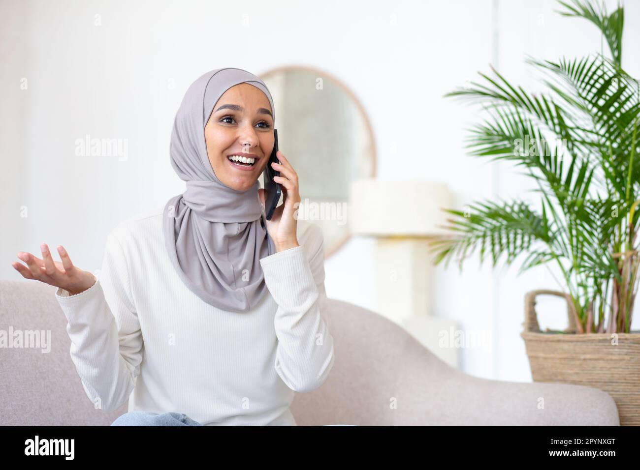 Young arab woman in hijab sitting on sofa at home and talking on the ...