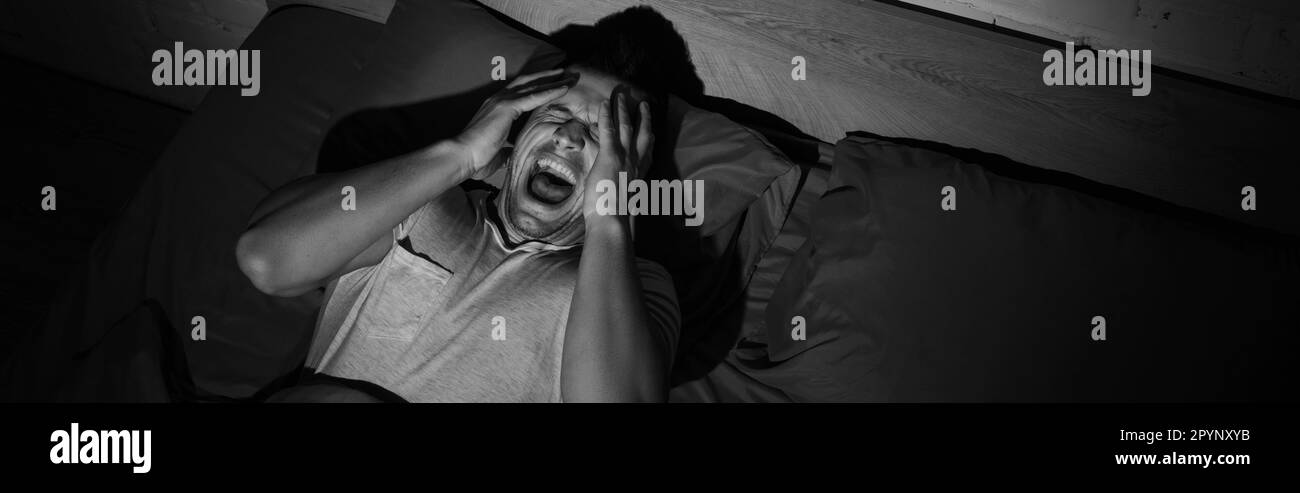 monochrome photo of young man screaming while having nightmares and panic attacks at night, banner,stock image Stock Photo