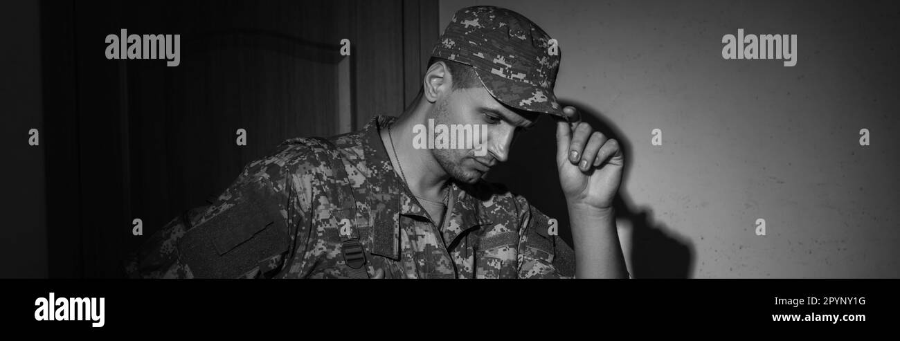 Black and white photo of upset soldier in uniform standing in hallway at home at night, banner,stock image Stock Photo