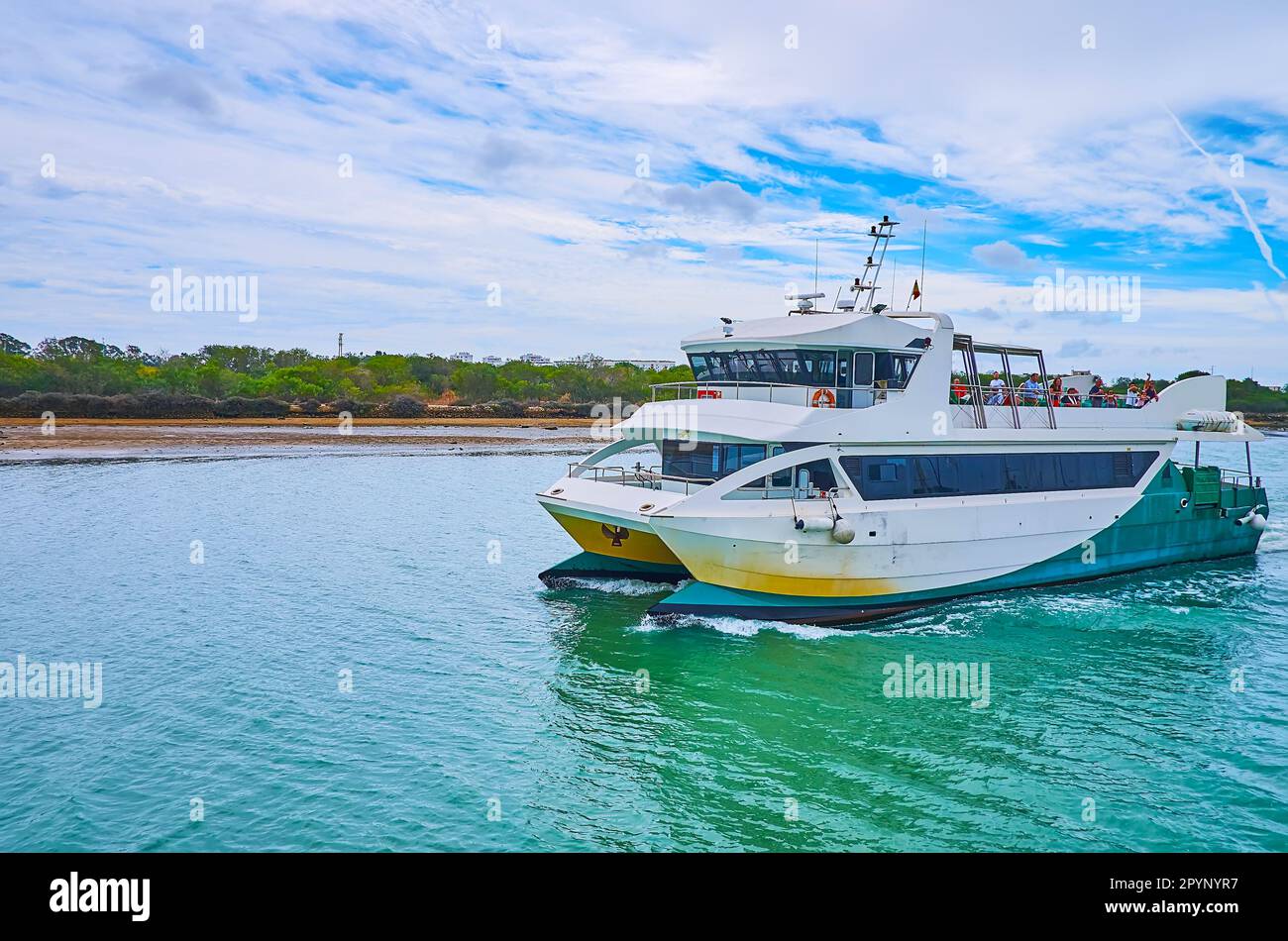 The passenger ferry floats along the green bank of Guadalete River to
