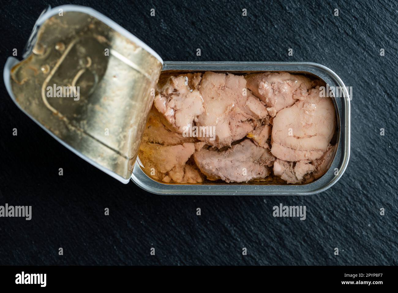 Open tin can with cod liver on black background, close up, top view ...
