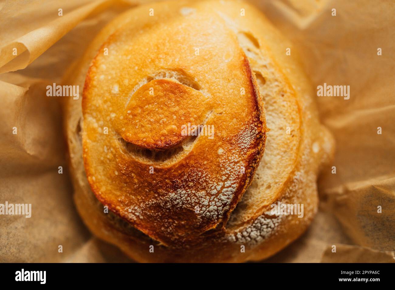 Freshly baked round loaf of homemade sourdough bread on brown parchment paper, eye design Stock Photo